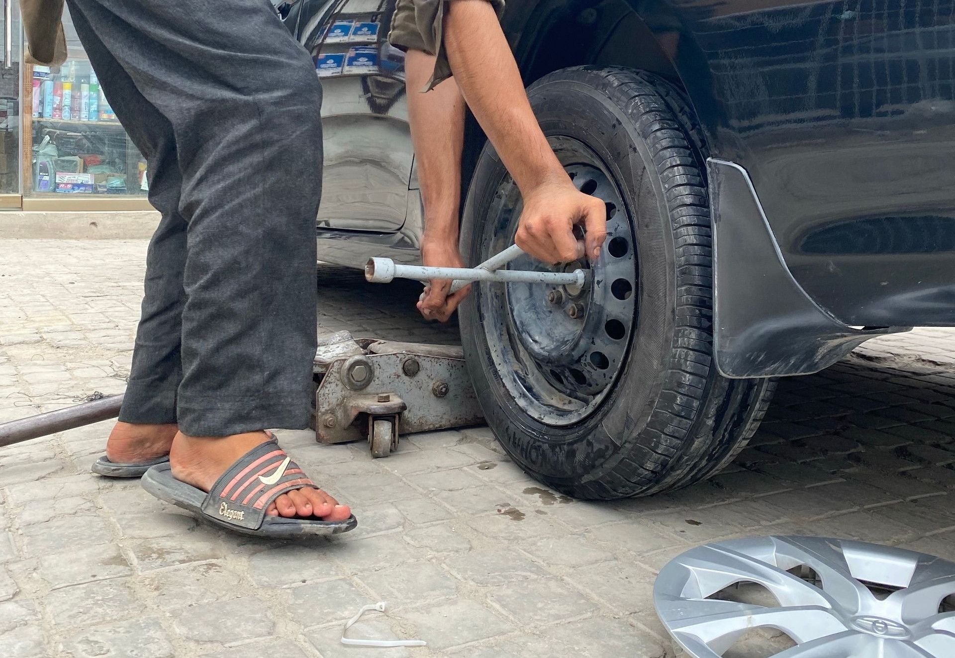 A young mechanic uses a lug wrench to fix a car tire outdoors.